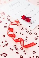 San Valentín día. rojo cinta en el formar de un espiral, seco flores y un calendario hoja para febrero en un rosado antecedentes con corazones. vertical ver