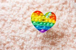 Silicone rainbow antistress toy in the shape of a heart on a background of fluff. Trendy relaxation tool photo