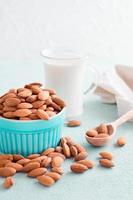 Peeled almonds in a bowl and almond milk in a glass on a light background. Alternative nutrition, source of vitamins. Vertical view photo