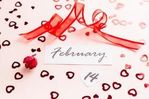 Valentine's Day. Date 14 february and red ribbon on pink heart-strewn background. Close-up photo