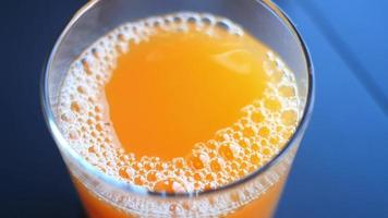 Haut vue de une verre de Orange jus avec la glace sur bleu Contexte video