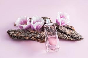 A gorgeous bottle of cosmetic or spray lies on parts of the bark of the tree and buds of spring lilac flowers. product presentation. photo