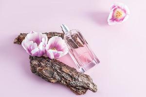 a chic bottle of women's perfume with a delicate floral aroma lies on part of the bark of the tree with spring flowers. aroma presentation. photo