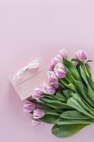 beautiful spring bouquet of tulips on a purple background with a gift box with a white ribbon. vertical view. space for text. photo