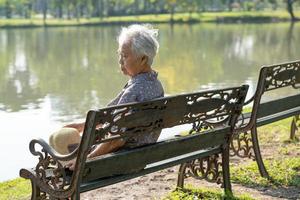 Asian elderly woman depressed and sad sitting back on bench in autumn park. photo