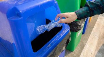 People hand throwing empty water bottle in recycle bin. Blue plastic recycle bin. Man discard water bottle in trash bin. Waste management. Plastic bottle garbage. Reduce and reuse plastic concept. photo