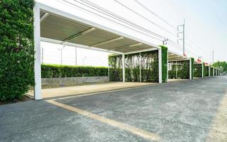 Empty car parking lot with green hedge tree fence. Parking zone on sunny summer day and empty space. Outdoor car parking lot with concrete floor. Eco-friendly outside parking lot. Modern architecture. photo