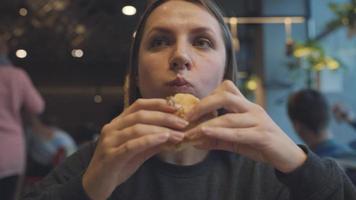 Woman eats a hamburger in a cafe video