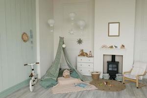 White fabric teepee and Scandinavian simple decor in the interior of the children's room. Children's bicycle, chest of drawers and fireplace with child seat photo