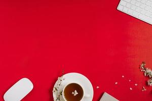 el lugar de trabajo de una bloguera con teclado de computadora, oficina, flores de manzano, té en una taza sobre un fondo rojo. endecha plana, vista superior, espacio de copia. concepto de primavera y día de san valentín foto