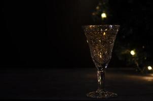 Glass with white wine with garland lights on the background. dark picture. Golden beverage in the glass. Beautiful lights reflected in the glass. photo