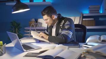 jong onderzoeker Mens lezing wetenschappelijk boek in zijn kantoor. jong Mens met bril is zittend in de helder studie kamer, lezing een boek en werken Aan een laptop. video