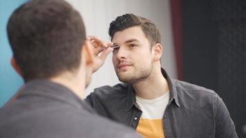 The young man who loves himself removes his eyebrows and the hairs he does not want to see with tweezers in front of the mirror. video