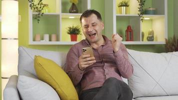 The man texting on the phone is having a happy and fun time with the person he is talking to. The man who is texting with people on his smartphone at home is laughing and having fun. video
