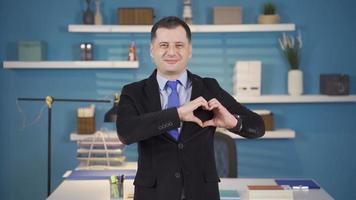 Businessman making heart with hands looking at camera. Happy and cute businessman makes heart with hands and smiles at camera. video