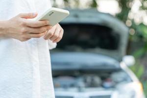 avería, coche roto, reparación. la mujer usa las primas de seguro de cheques de teléfonos móviles a través de la aplicación debido a un accidente automovilístico. encuentre un garaje para arreglar el automóvil durante la gira por el país, esperando ayuda, emergencia. foto