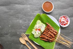 chicken satay or chicken satay served with lontong, rice cake and peanut sauce. served on banana leave photo