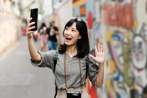 Young Asian woman backpack traveler using mobile phone, enjoying street cultural local art wall. Traveler checking out side streets. photo