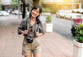joven asiático mujer mochila viajero disfrutando calle cultural local sitio y sonrisa. viajero comprobación fuera lado calles foto