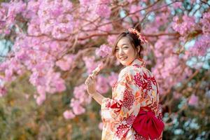 asiático mujer vistiendo kimono disfraz y participación dango con Cereza flores foto
