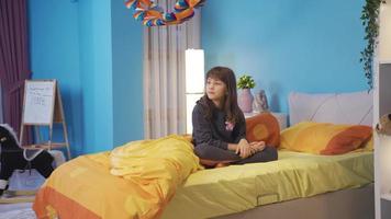 The beautiful little girl who does not sleep in her bed is thoughtful, she has a problem. Worried and stressed little girl sitting thoughtfully in her room alone video