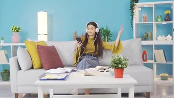Young girl listens to music with headphones at home. Cheerful and beautiful young girl sitting on sofa at home and listening to music. video