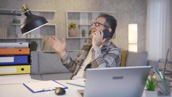 Mature man working in home office talking on the phone and is happy. Mature man talking on the phone is working in his home office and is happy. video