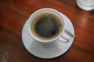 A mug of hot black coffee stands on a wooden table. White mug with coffee photo