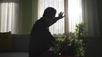 Worried pensive old man sitting alone at home, thinking about life alone. Depressed unhappy old man with health problems in old age feeling lonely. video