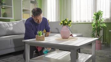 een middelbare leeftijd Mens wie reinigt de huis gedurende de dag en maakt alles fonkeling. volwassen Mens afvegen meubilair en verdieping in modern leven kamer met stofdoek. schoonmaak ziekte. video