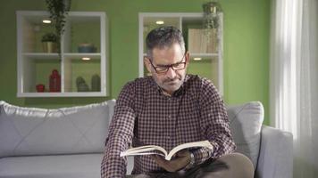 content Sénior mature homme relaxant sur canapé tandis que en train de lire une livre à maison. retraite, Accueil vie, mode de vie concept. video