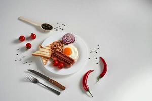 Traditional English Breakfast. Plate with Fried egg, two fried sausages, grilled bread toast, canned beans, blue onions and cherry tomatoes on a White Background. Copy space photo