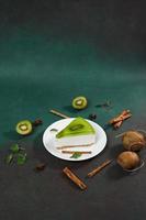 Cheesecake with Kiwi, cinnamon stick and leaves mint on a green background. Copy cpase for text photo