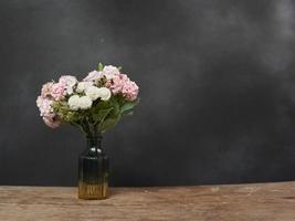 Vase with pink and white Flowers Stands on a Wooden Table against a Black blurry Background. Copy space for text photo