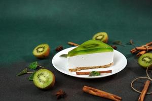 Cheesecake with Kiwi, cinnamon stick and leaves mint on a green background. Copy cpase for text photo