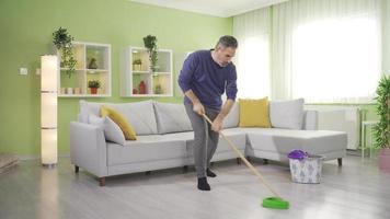 di mezza età uomo fare lavori di casa, rastrellamento piani nel vivente camera. un' maturo uomo mop pavimento superfici a casa, praticante bene igiene abitudini per mantenere un' pulito vivente spazio. video