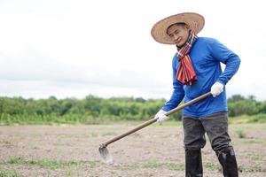 asiático hombre granjero es laboral, sostiene un azada a cavar suelo. concepto, agricultura ocupación, utilizar tradicional herramienta a obtener eliminar hierba en lugar de utilizando productos quimicos eco simpático agrícola actividad. tailandés granjero foto