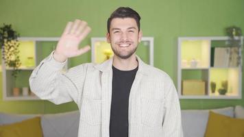 Young man waving at camera and happy. Happy cute young man looking at camera and waving at the same time. video