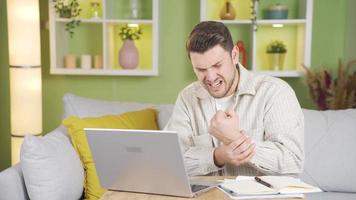 Young man has pain in his wrist while working from laptop and it hurts. Young man who pauses and painstakingly exercises his wrist due to wrist pain while on the job. video