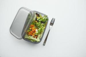 parte superior ver de un almuerzo caja con Fresco ensalada en blanco mesa foto