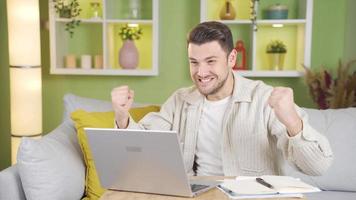 giovane uomo urla con gioia a che cosa lui vede su il schermo mentre Lavorando a partire dal il computer portatile. video