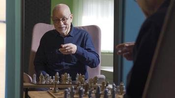 Lonely old man playing chess alone at home out of boredom. Depressed old man plays chess alone to spend time at home and gets sad thinking of his loneliness. video