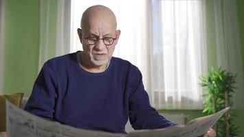 Depressed and lonely old man reading newspaper to spend time at home. The old-fashioned old man reads the newspaper alone at home, sees the news and current events in the newspaper. video