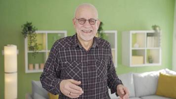 divertimento e divertente vecchio uomo è danza a casa, lui è nel bene spiriti e contento. divertimento e carino vecchio uomo danza guardare a telecamera a casa. video