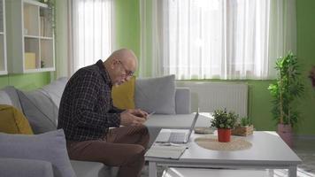 velho homem trabalhando às casa em computador portátil, fazendo pesquisar, escrevendo correspondência. idosos homem às casa olhando às computador portátil a sério e focado e considerado. video