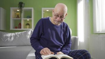 culto velho homem lendo às lar, feliz e pacífico. a velho homem é lendo dele livro sozinho às casa em uma ensolarado dia e é feliz. a velho homem relaxa e encontra paz. video