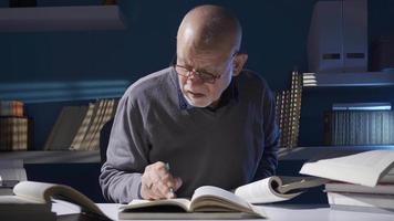 wijs oud Mens lezing een boek, onderzoeken historicus volwassen Mens. onderzoeker of historicus volwassen oud Mens lezing een boek, nemen aantekeningen terwijl werken in zijn studie. video