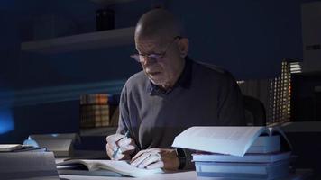 investigador ou historiador maduro velho homem lendo uma livro, levando notas enquanto estudando às lar. velho homem dentro óculos lendo uma livro, fazendo pesquisar, pensando dentro dele trabalhos escritório. video