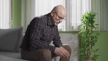 Lonely old man inside sitting alone at home. Thoughtful retired man. Unhappy and sad old man sitting on sofa thoughtful and moody at home. video