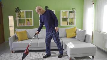 Old man cleaning house gets tired while using vacuum cleaner. The old man has trouble cleaning the house due to his health problems and age. video